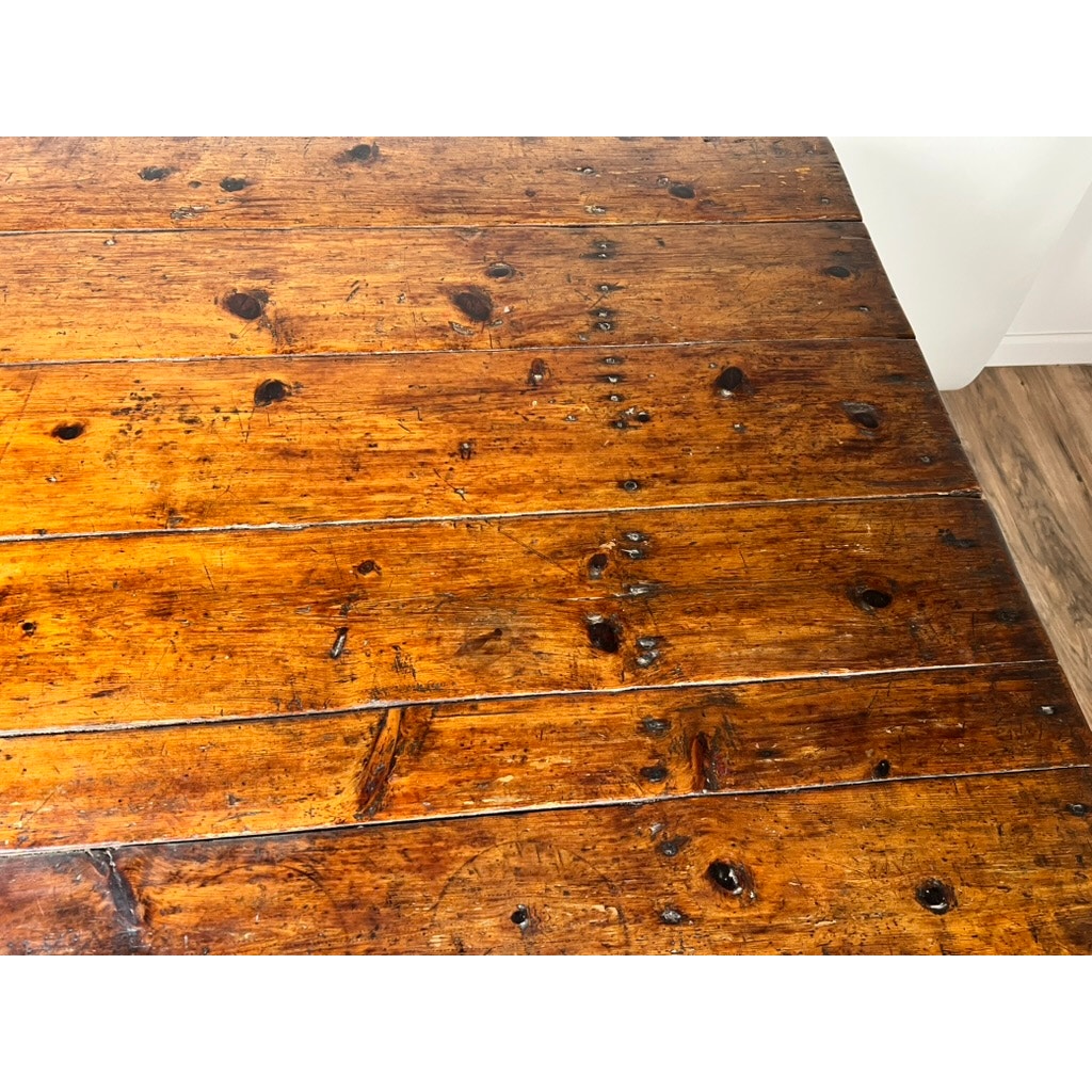 Close-up of the Antique Country Pine Hutch Table with a six-plank top: its shiny surface shows visible grain, dark knots, and imperfections that evoke 18th-century charm. The table sits on a lighter wood floor near a white wall.