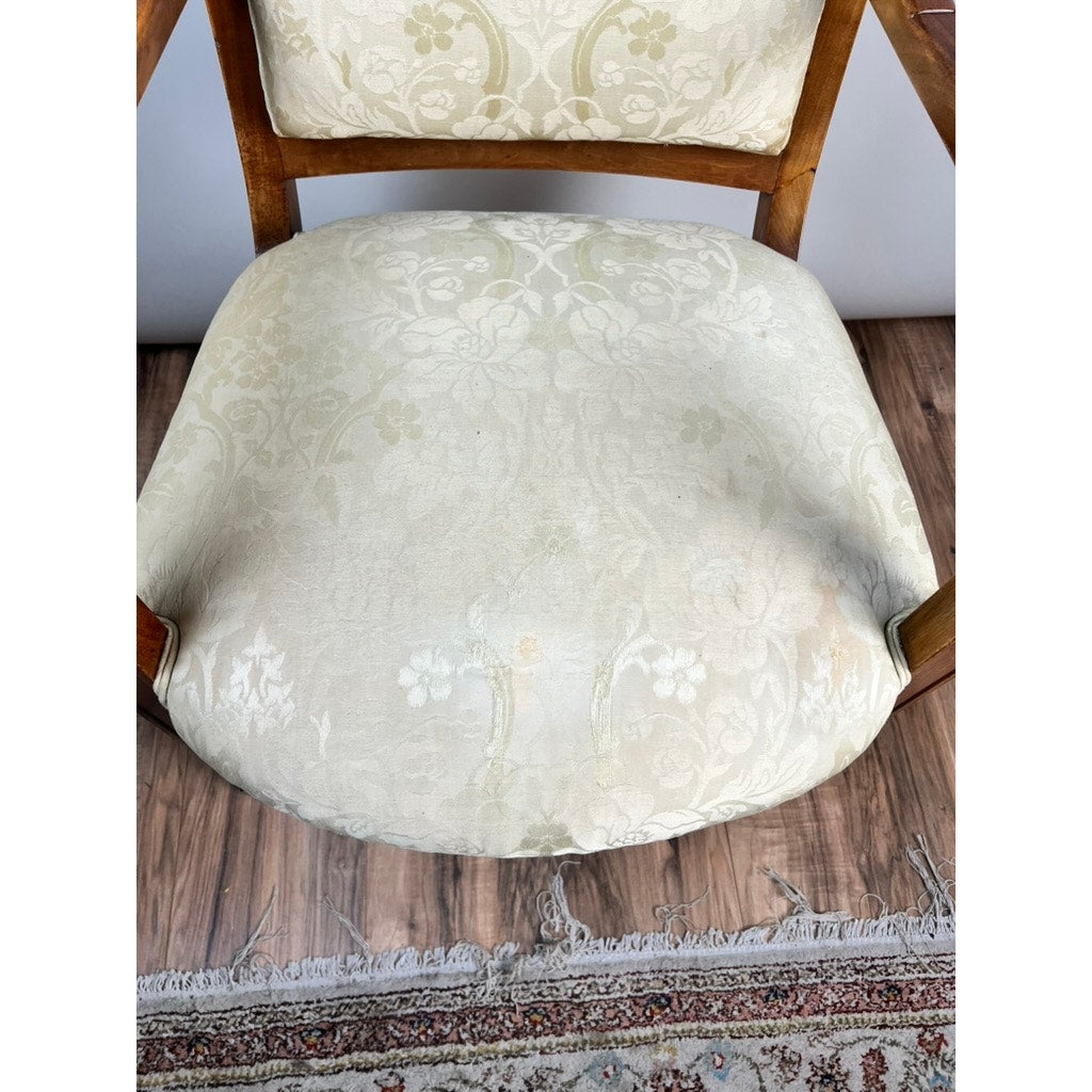 An Antique French Directoire Style Fauteuil Open Arm Chair in Sapelle Mahogany (late 19th c.) features an off-white upholstered seat with light patterns, showing some wear. A fringed rug is partially visible on the wooden floor below.