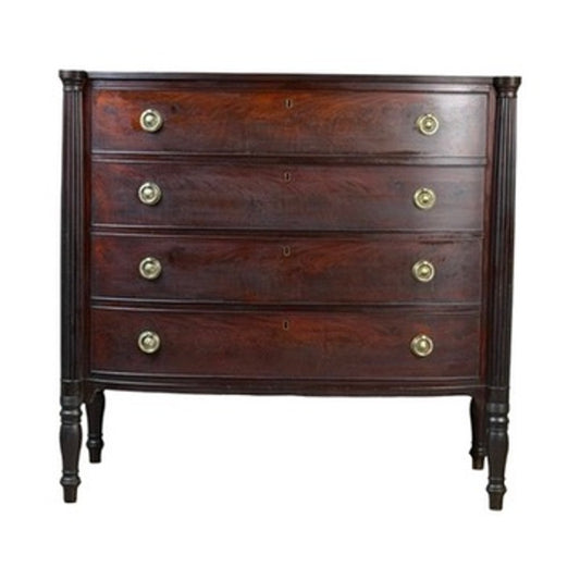 This Early 19th Century New England Federal Mahogany Bow-Front Chest of Drawers (c. 1810–1825) features four gracefully curved drawers, each fitted with two round brass handles. Slender turned legs and a rich dark brown finish highlight the timeless elegance characteristic of Federal-era furniture.