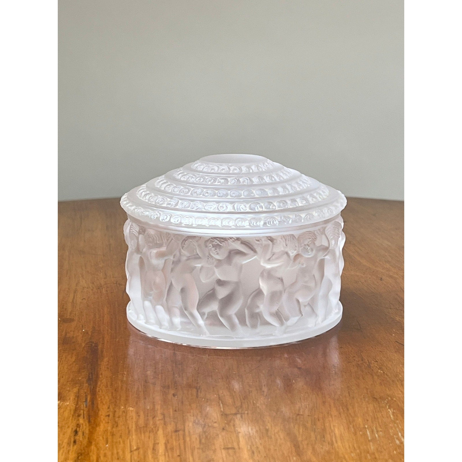 The Vintage Lalique Crystal Enfants Box by Lalique is a round, white frosted glass trinket box with a domed lid featuring raised dancing figures, inspired by French art glass.