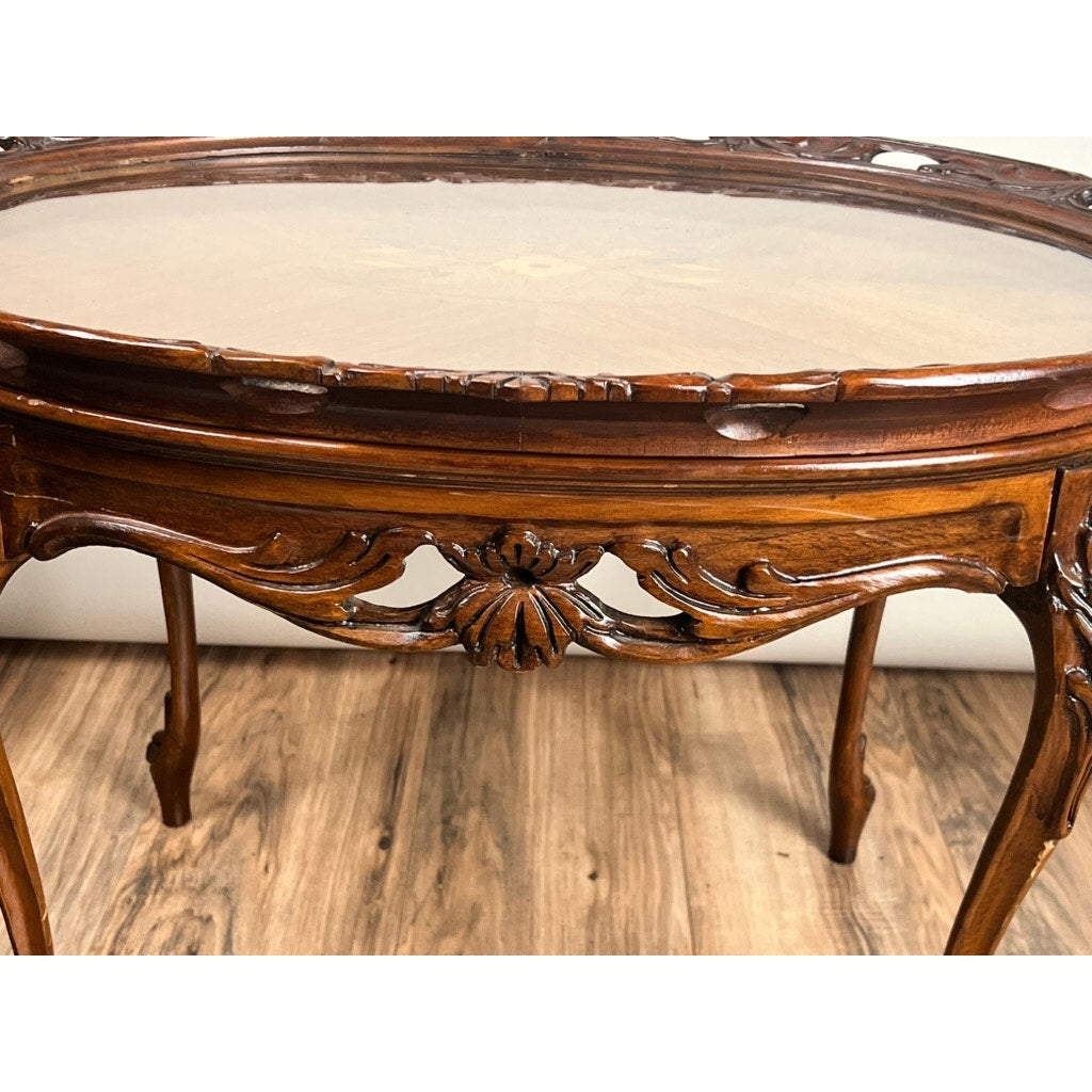 A close-up of a Vintage Louis XVI Style Butlers Table with removable glass tray, featuring ornate carved floral and leaf details, set on a wooden floor against a white background. Brand: None or unknown.