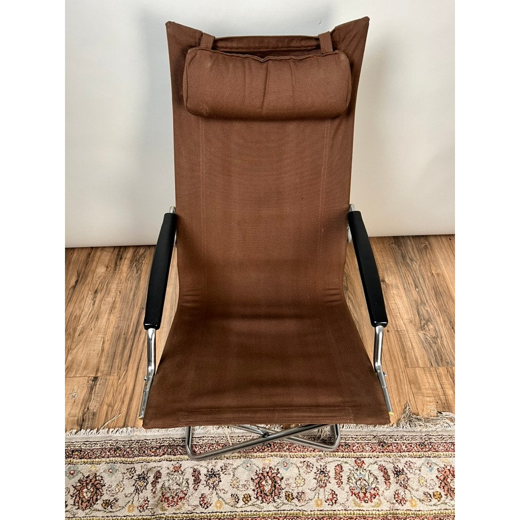 A Vintage Uchida Z Chair Japanese Modern Chrome Sling Lounge Chair with Headrest by Uchida, featuring a brown high-back design with chrome metal legs and black armrests, sits on a patterned rug over wooden flooring against a plain white wall—an elegant example of Japanese modern design.