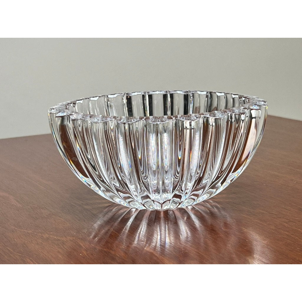 A Tiffany & Co. Vintage Crystal Bowl with a ribbed petal design sits on a polished wooden surface, evoking timeless elegance against a plain backdrop.