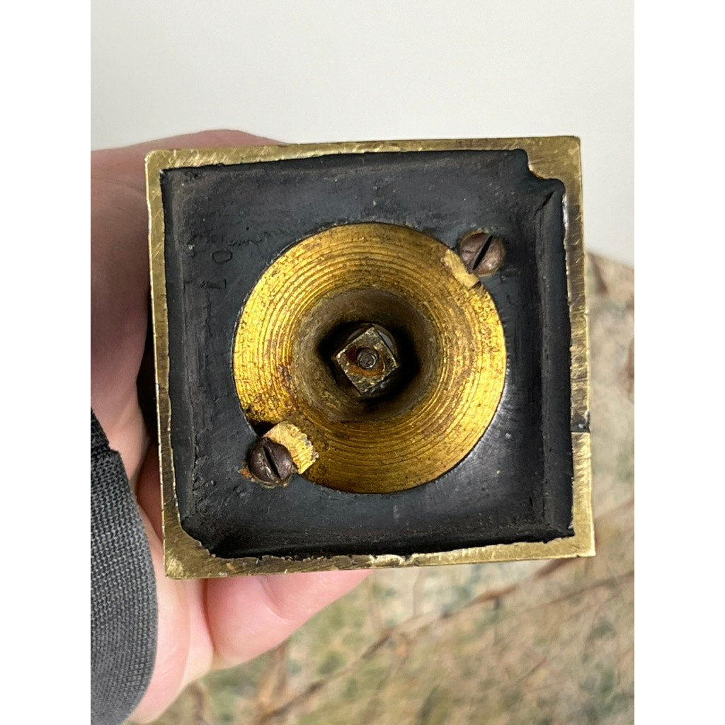 Close-up of the underside of an Antique Small Bronze Bust of King Menelaus (late 19th Century), showing a square base with a hexagonal hole, two screws, black frame around the brass, and a hand holding the piece. Brand unknown.