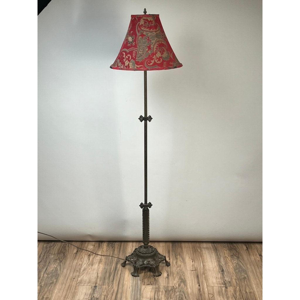 The Antique Art Deco Cast Iron Floor Lamp by Rembrandt features a decorative cast iron base and a red lampshade with gold floral patterns, shown standing on a wooden floor against a plain backdrop.