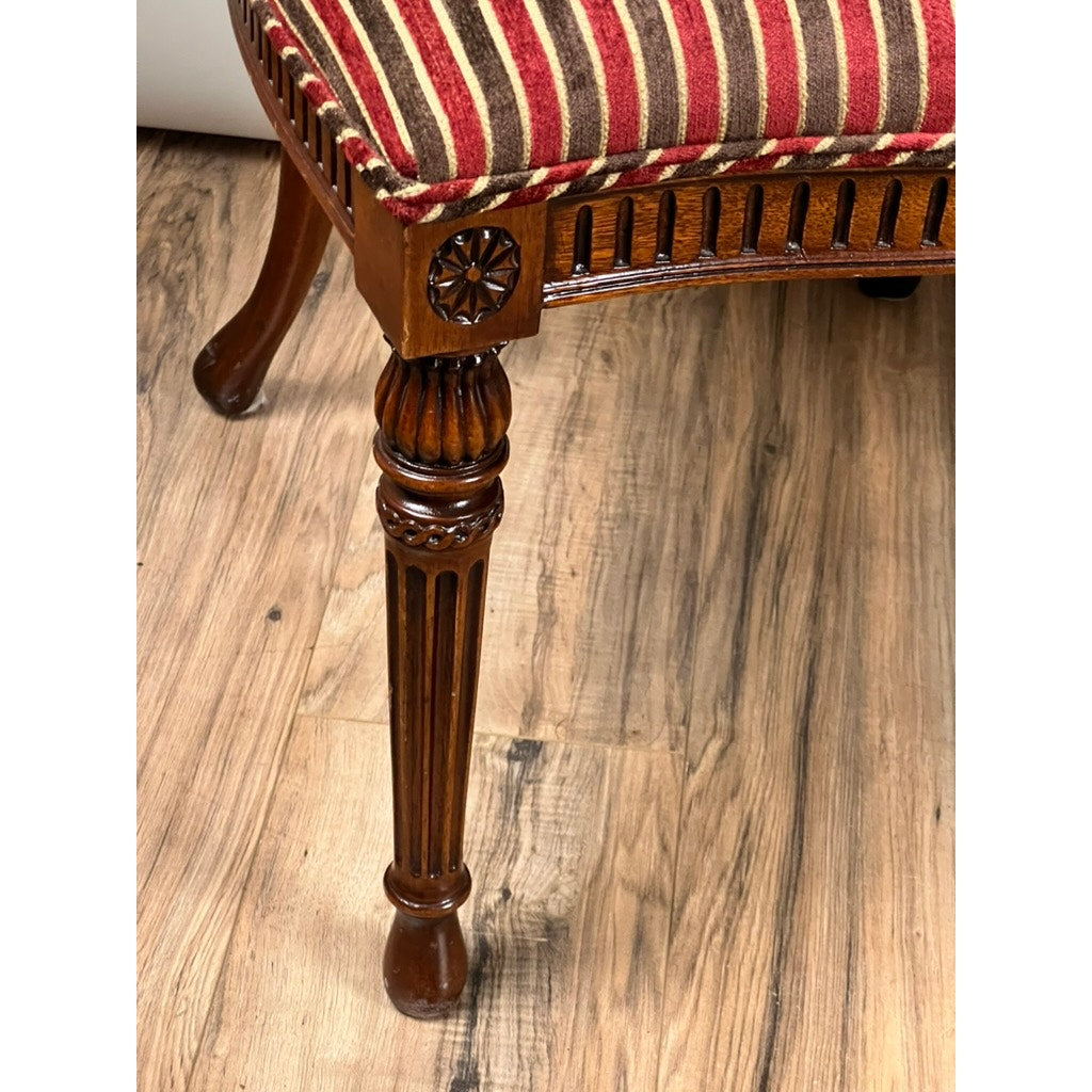 Close-up of a Vintage Pair Wheel Back Side Chair by Ardley Hall, showing its carved wooden leg with a decorative flower motif and red, beige, and brown striped upholstery on a wood-patterned floor.