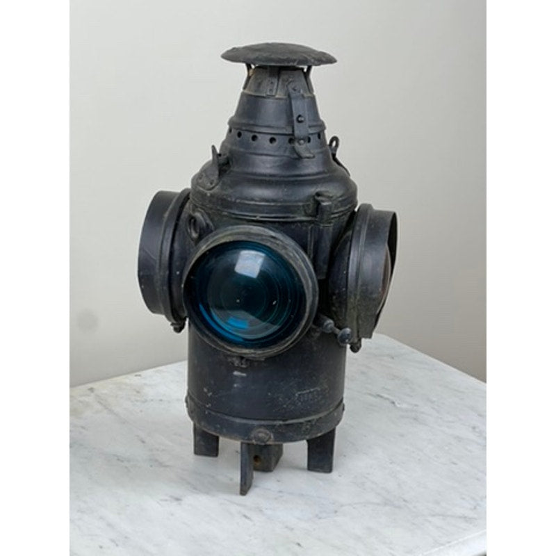 Antique Illinois Central Railroad Signal Lantern by Dressel Arlington NJ—a vintage black metal lantern with blue glass lens and two side openings, displayed on white marble against a plain light wall.