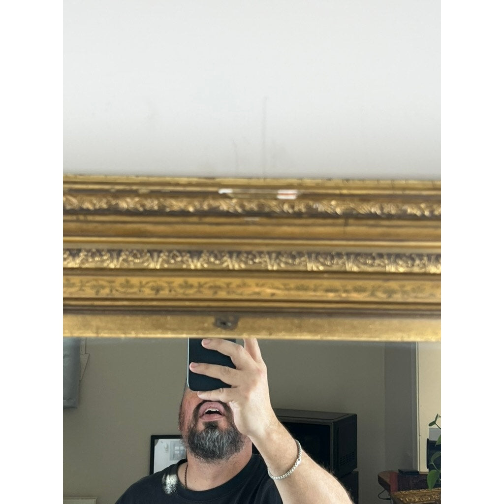 A bearded person takes a mirror selfie, holding their phone in front of their face. The Fine Antique 19th Century Gilt Wood Mirror (39 x 34) with an ornate gold frame only partially reflects their face and upper body.