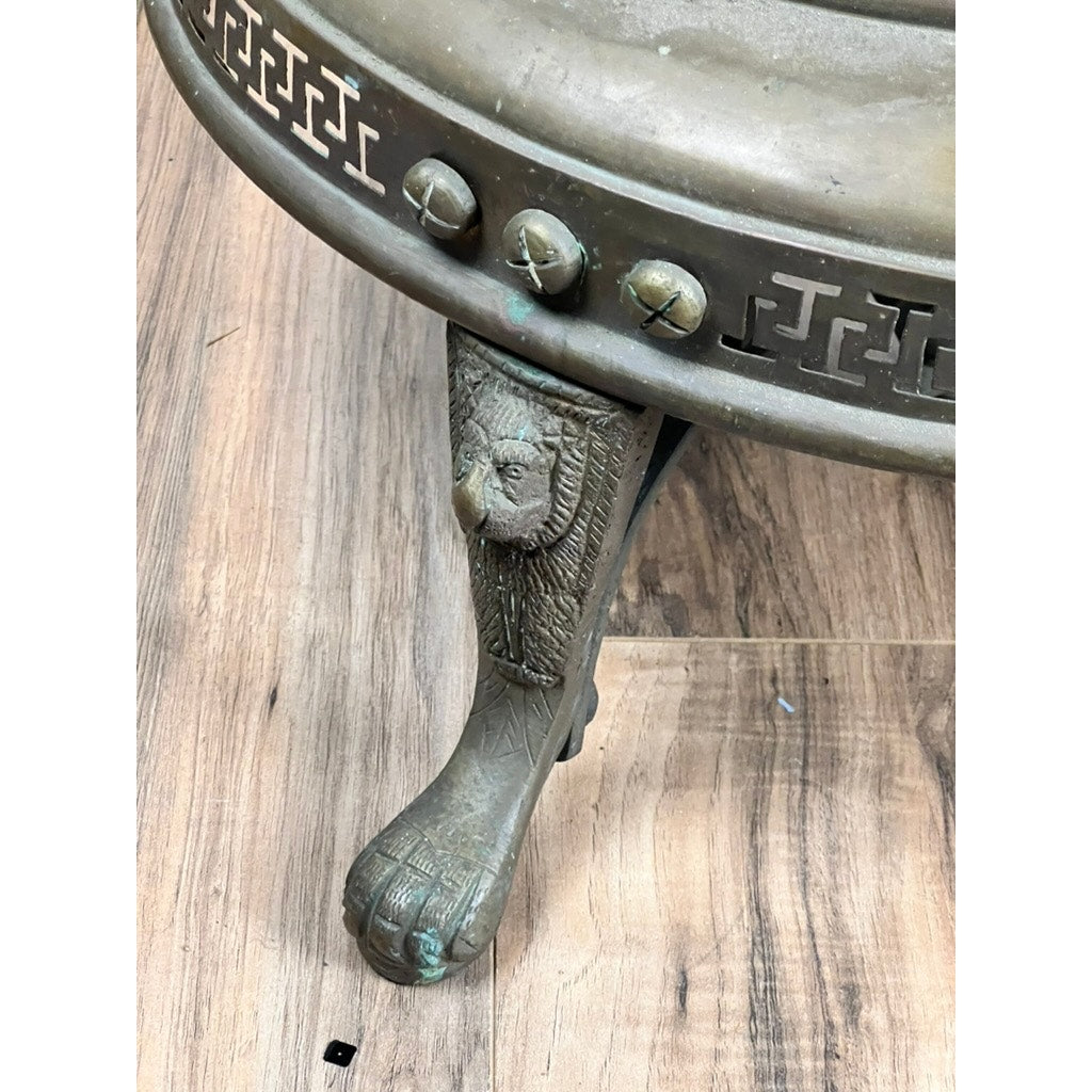 Close-up of an Antique Venetian Brass Bell Room Heater Brazier (19th Century) with ornate details, including a sculpted lion’s paw and face leg, Greek key patterned rim, and decorative studs, resting on a wooden floor. Brand unknown.