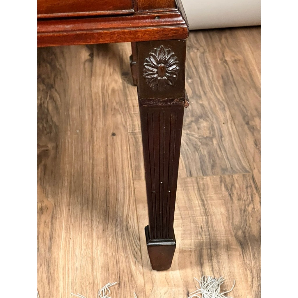Close-up of an Antique Directoire Style French Cylinder Desk leg, c. late 19th century, featuring carved floral and vertical details on wood, set on a wood-patterned floor with part of a carpet fringe in view.