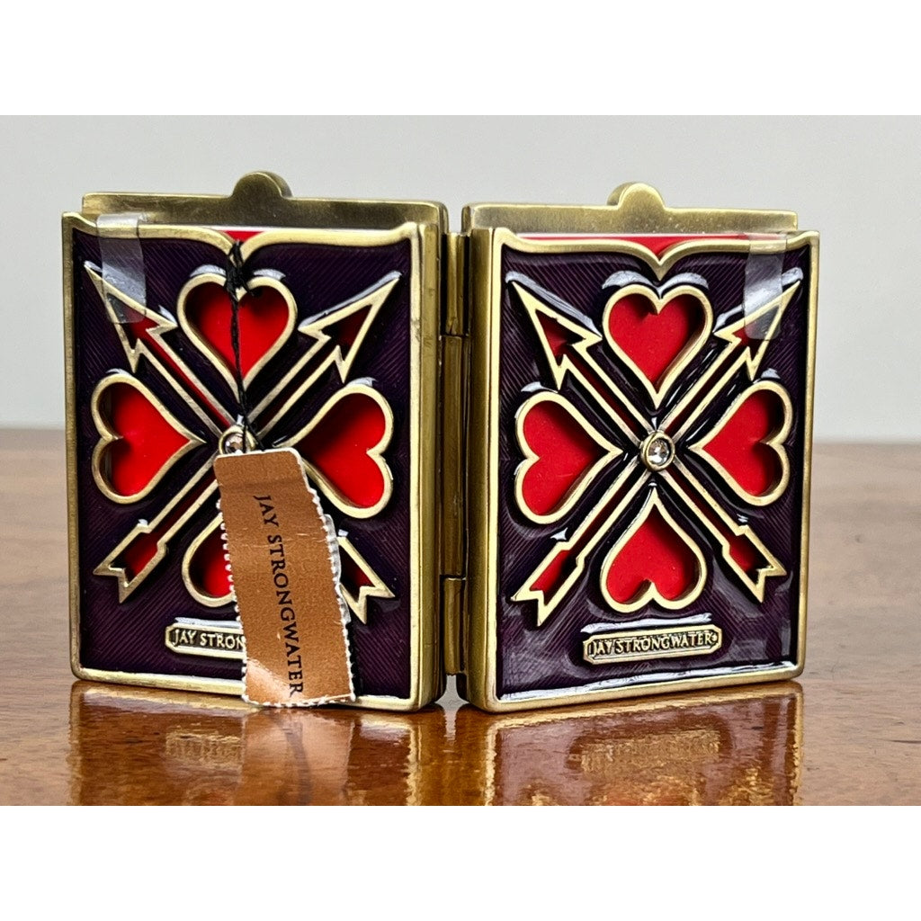 A New in Box Jay Strongwater Bejeweled Enamel Double Heart Picture Frame, featuring gold and red hearts with sparkling accents, is displayed on a wooden surface, accompanied by a tan tag showing the Jay Strongwater brand name.