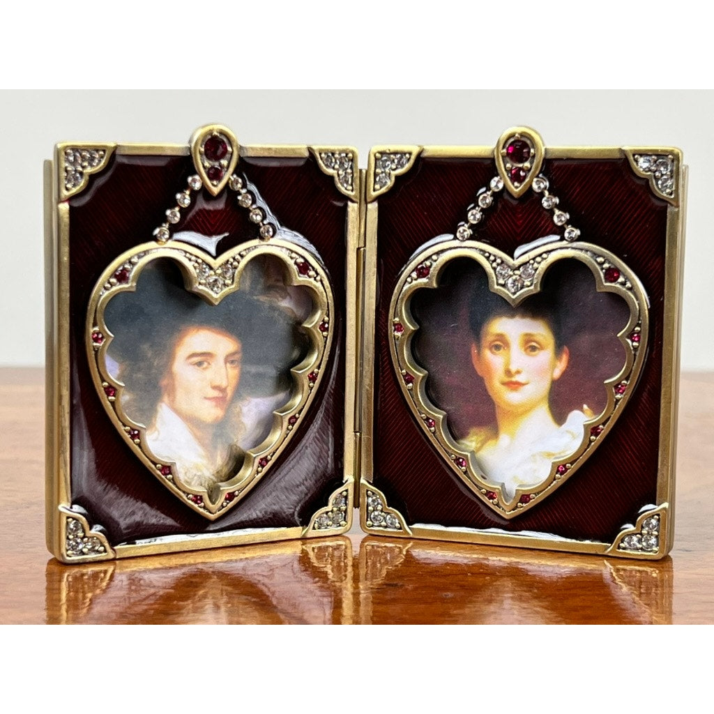 The Jay Strongwater Bejeweled Enamel Double Heart Picture Frame features two heart-shaped frames on a red and gold jeweled background, perfect for displaying portraits. New in box.