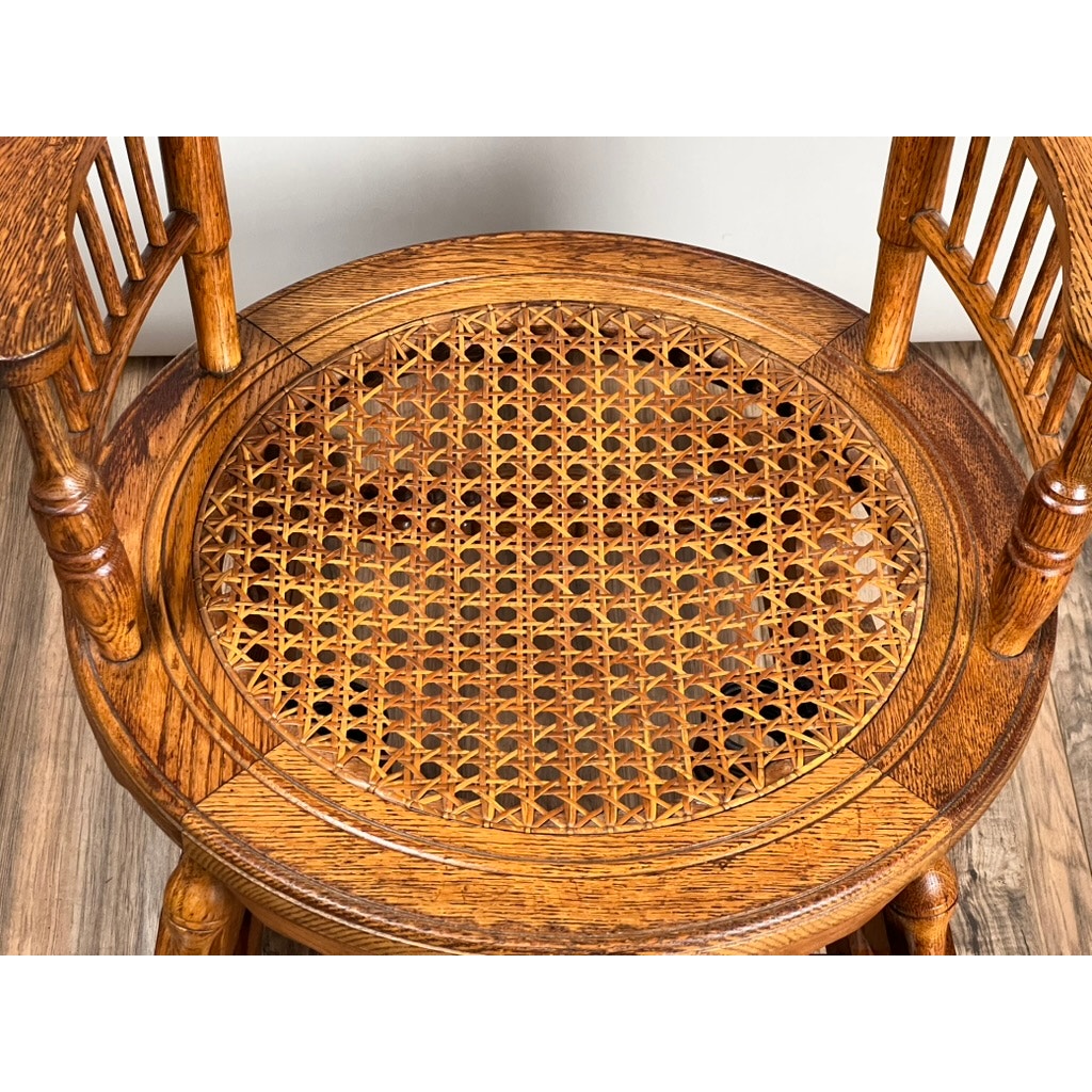 An overhead view of the Antique Victorian Oak Platform Rocker (c. Late 19th Century) with a round cane seat, curved spindle armrests, and intricate wood grain, showcasing detailed 19th-century craftsmanship on a wooden floor. Brand: Unknown.
