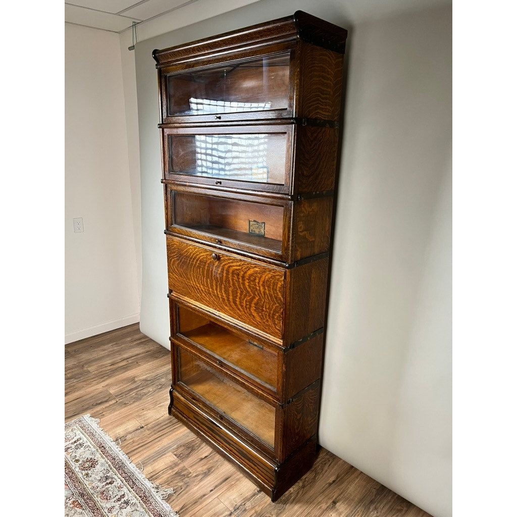 Antique Globe-Wernicke Quarter Sawn Oak 6-Stack Barrister Bookcase Secretary Desk, crafted circa 1905–1915, stands tall with six glass-fronted sections. Made from richly grained quarter-sawn oak with a dark finish, this elegant piece from Globe Wernicke rests on a wood floor beside a white wall and patterned rug.