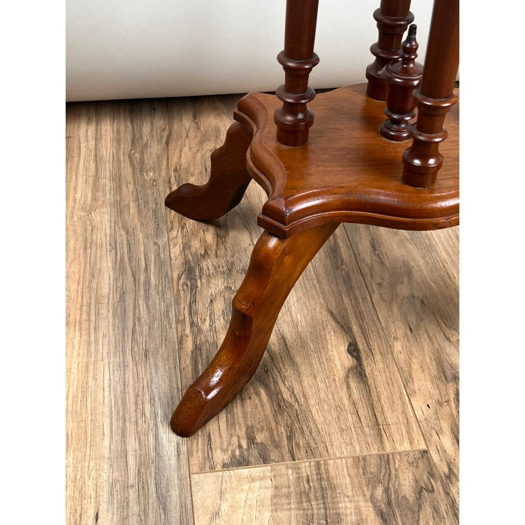 Close-up of the leg of an Antique Victorian Walnut Turtle Top Candle Stand (late 19th century) with ornate carving and glossy finish, shown on a light brown wood floor against an out-of-focus plain background.