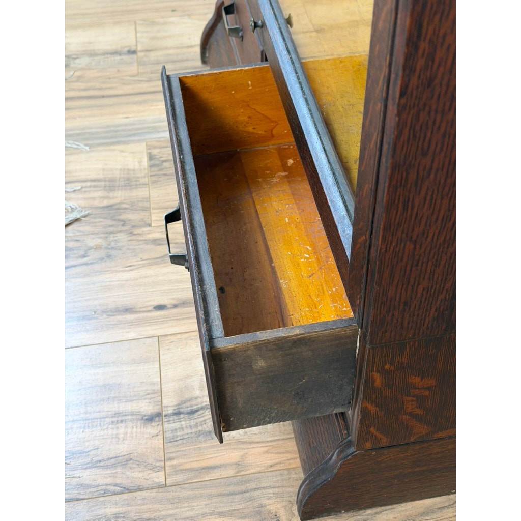 An open drawer in a Camden Cabinet Company Antique Hale System Quarter-Sawn Oak Five-Stack Barrister Bookcase, c. 1910, reveals an empty interior marked by visible scratches and signs of wear. The dark wood cabinet is set on a light wood floor.