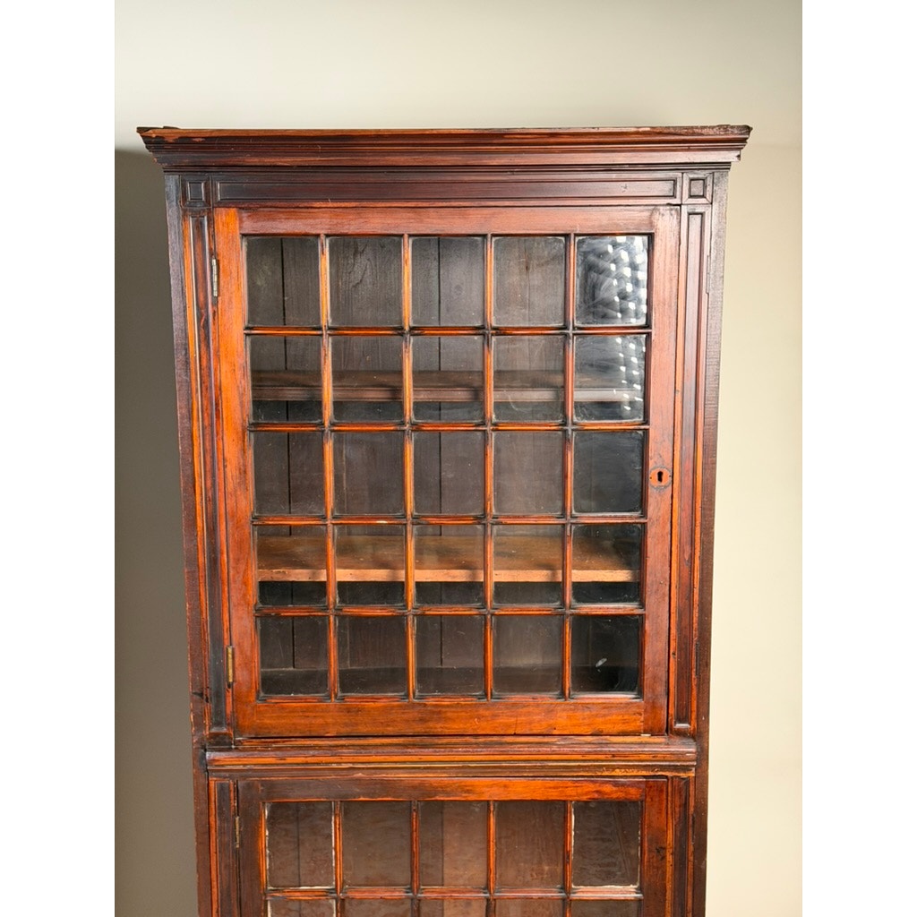 A pair of mid-19th century New England cherry glazed display cupboards by Pearl City Antiques (c. 1840–1860) features glass-paneled doors with a grid-like design on the upper sections, reminiscent of period cupboards. The empty shelves inside are visible through the dark, polished cherry wood framed by simple decorative trim.