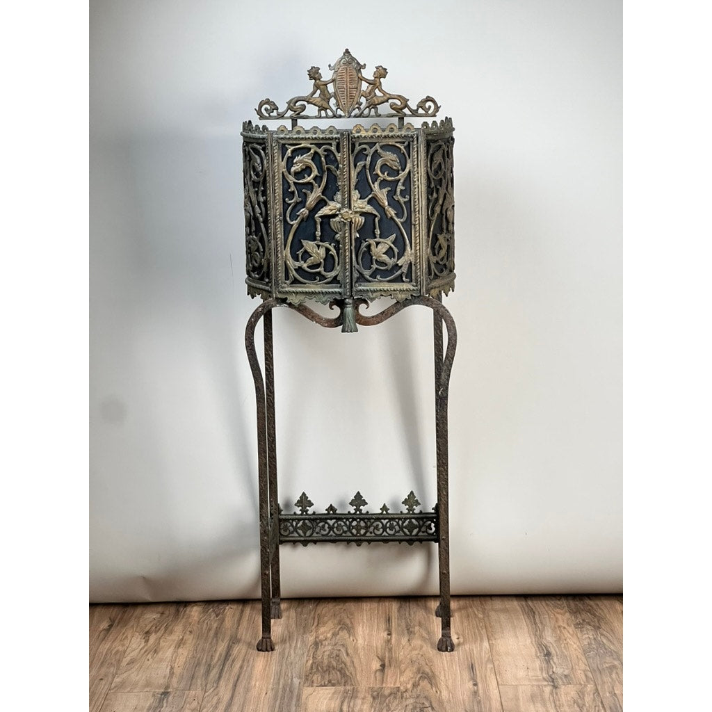 An Antique Gothic Revival Cast Iron and Brass Phone Stand, attributed to Oscar Bach or Bertram Segar c. 1920 Greenwich Village, stands tall on slender legs against a plain background on a wooden floor. Brand: None/Unknown.