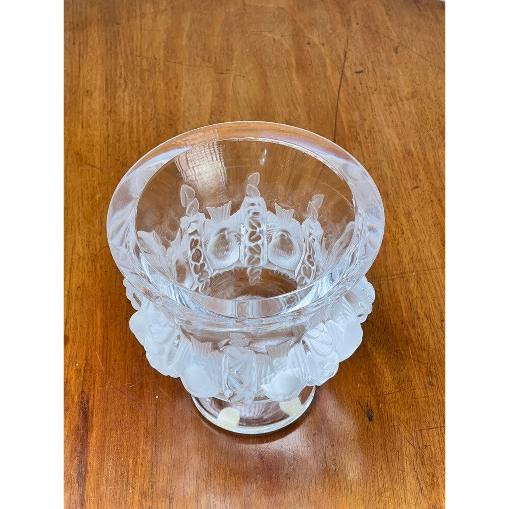 The Vintage Lalique Dampierre Sparrow Footed Vase by Lalique, featuring clear crystal with frosted sparrow details encircling the middle, stands on a wooden surface and exemplifies classic French artistry.