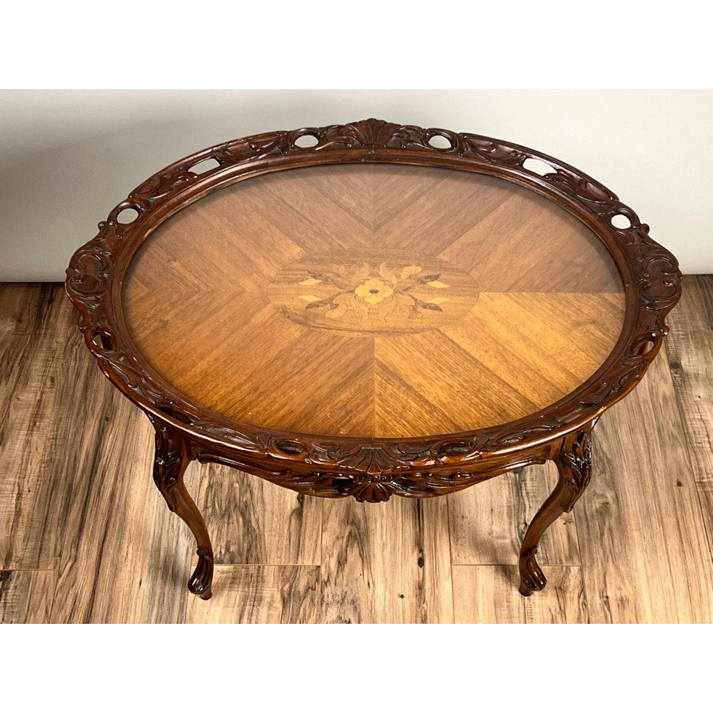 A Vintage Louis XVI Style Butlers Table with a removable glass tray top, ornate carved edges, and floral inlay at the center stands on four curved legs over a wooden floor. Brand: None/Unknown.