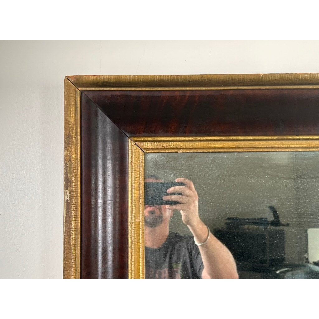 A person photographs their reflection in an Antique American Empire Parcel Gilt Flame Mahogany Ogee Wall Mirror (mid-19th c.); only the lower face is visible, and a plain wall forms the background. Brand: Unknown.