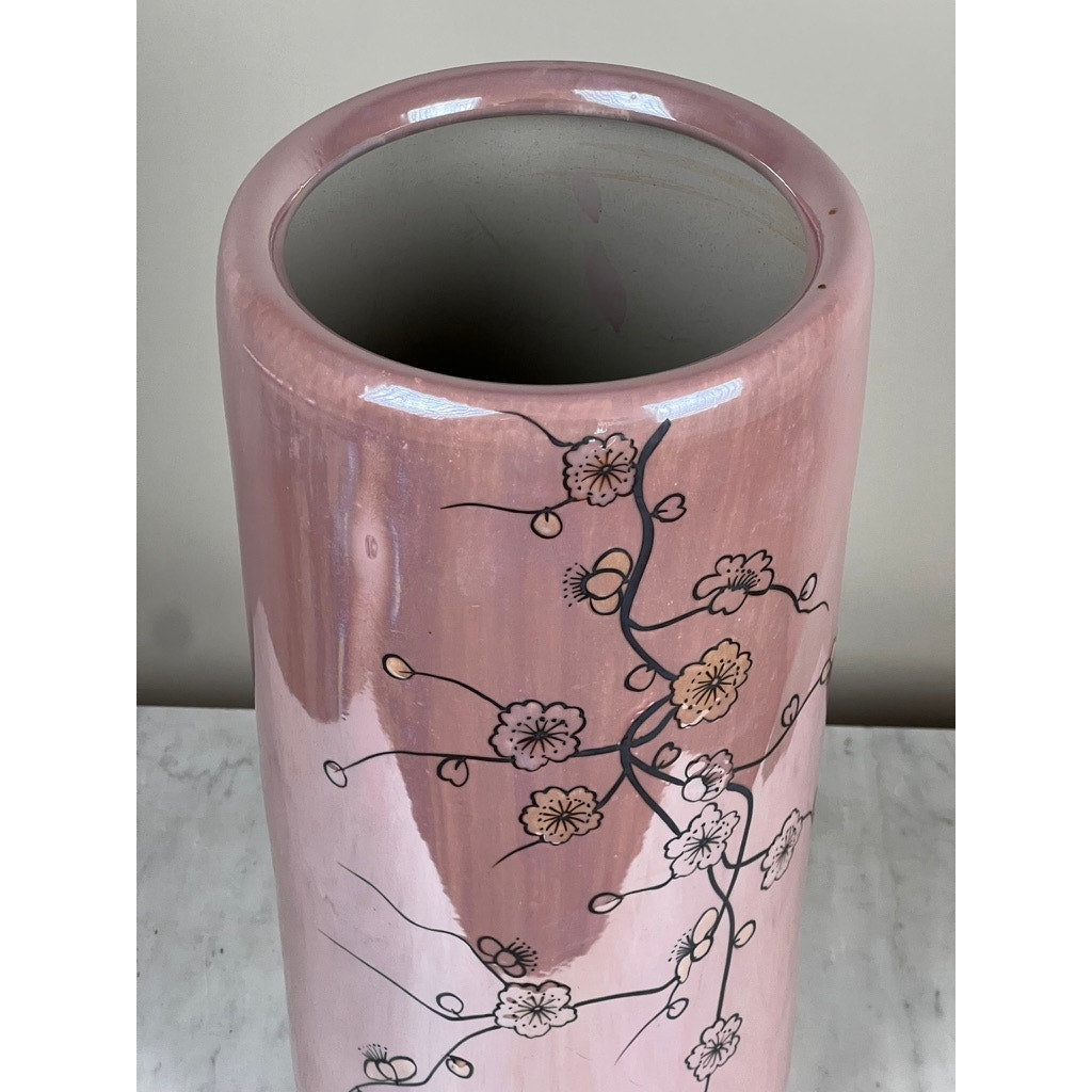 The Vintage Sakura Style Cherry Blossom Tall Vase features a glossy pink finish, wide opening, and is adorned with black branches and white-yellow blossoms. It sits elegantly on a light marble surface against a neutral background.