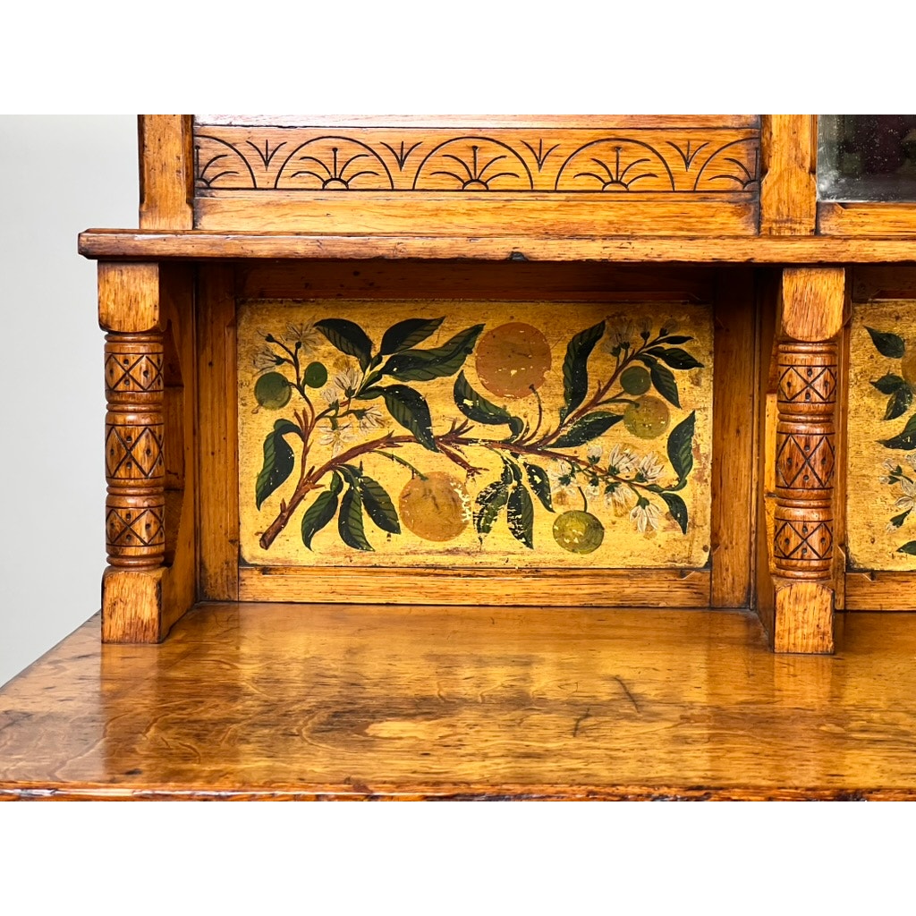 A close-up of an Antique Victorian Aesthetic Movement Oak Desk in Original Finish c. Late 19th Century, featuring carved columns and a painted panel of green leaves and yellow fruit on a warm, honey-colored oak background.