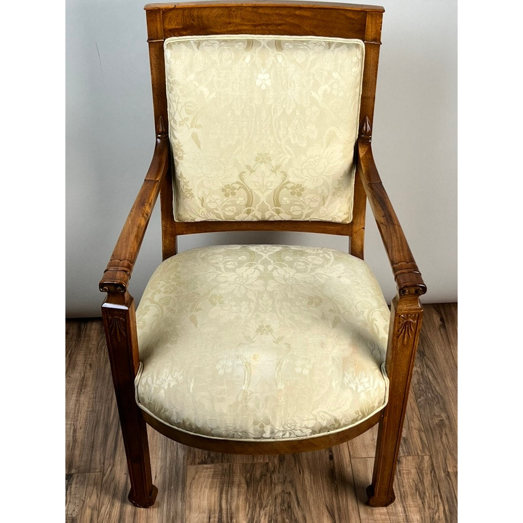 An Antique French Directoire Style Fauteuil Open Arm Chair in Sapelle Mahogany (late 19th century) with carved details, upholstered in light cream floral fabric, is placed on a wooden floor against a plain light background.