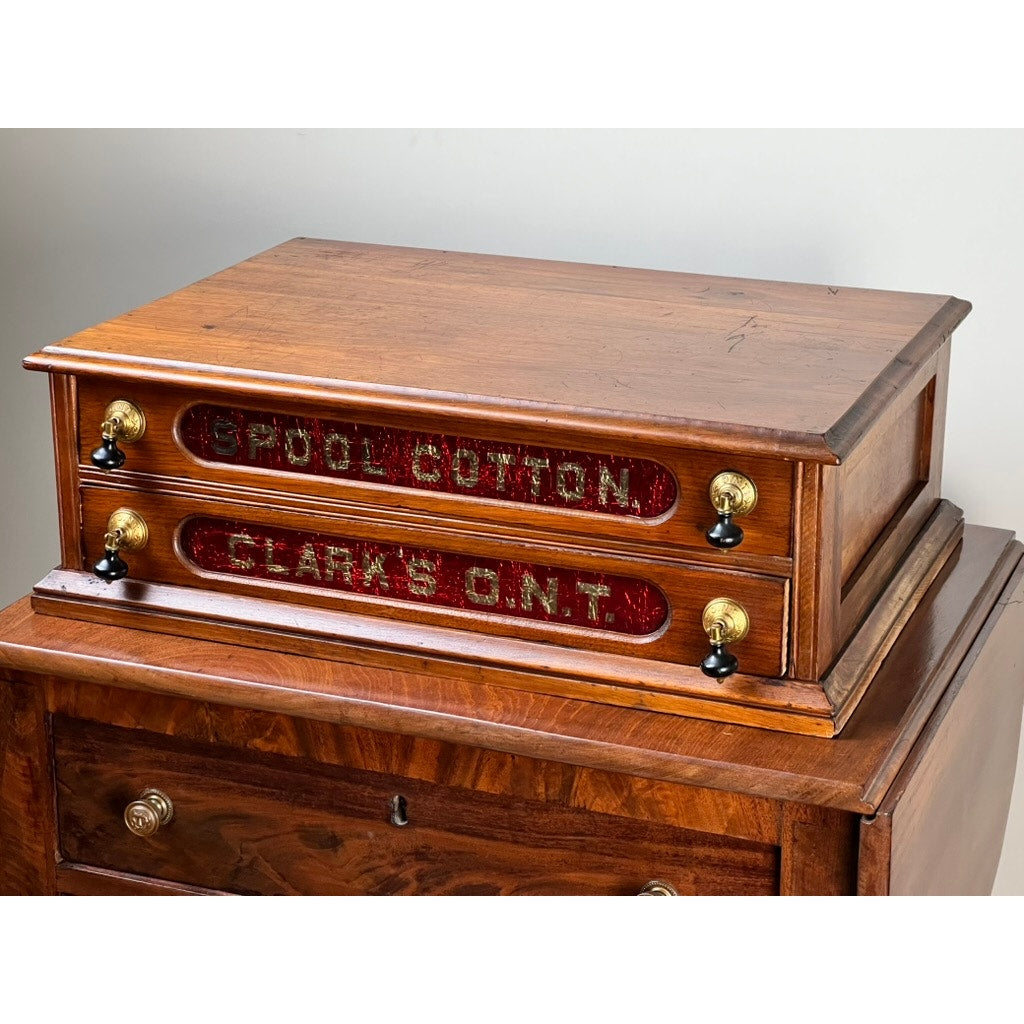 An Antique Victorian Pine Two Drawer Clark’s ONT Spool Cabinet c. Late 19th Century features red-labeled drawers, brass knobs, and black handles—a charming collectible from Clark’s ONT.